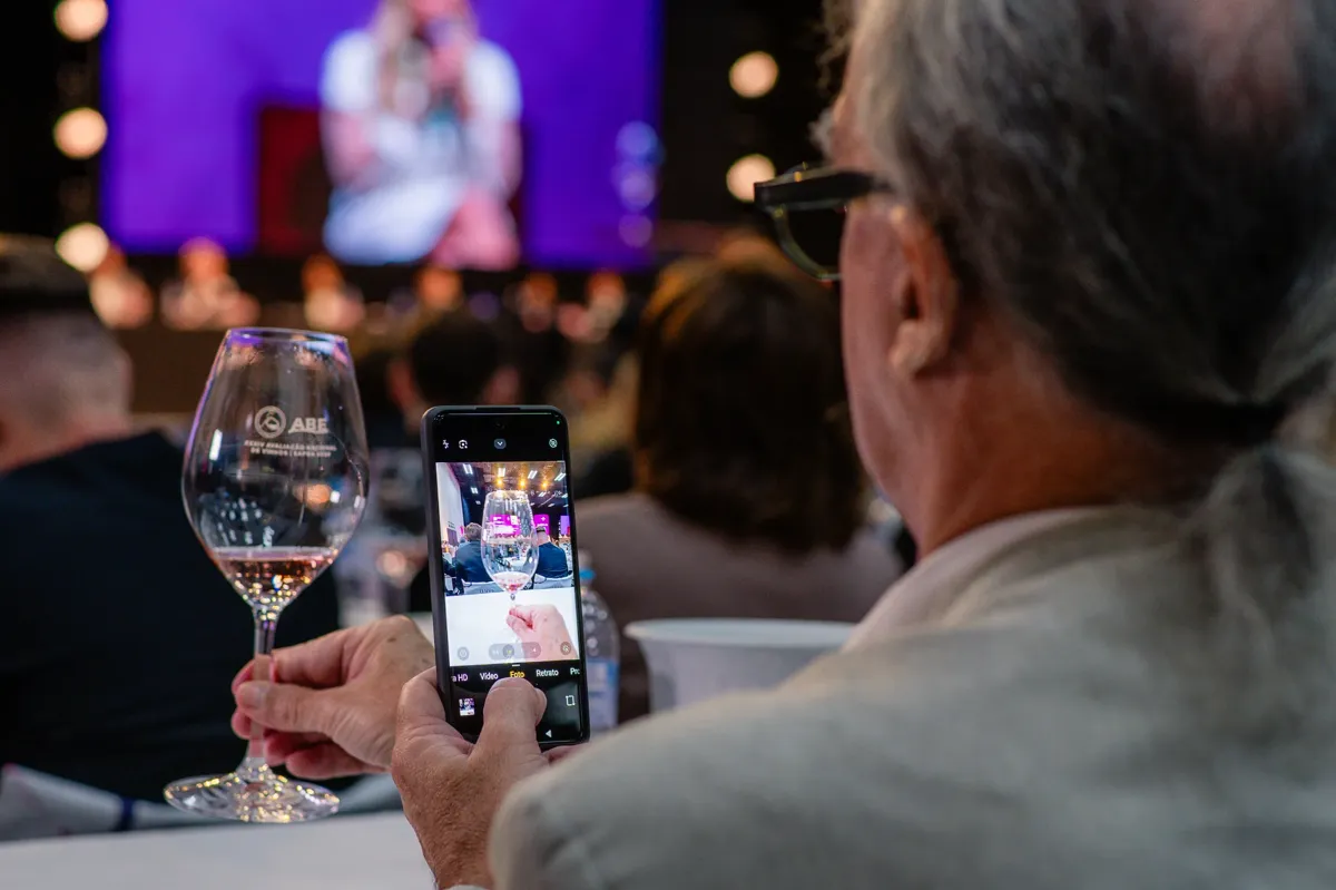 Homem tirando foto com celular da sua taça de vinho na ANV 2026.webp